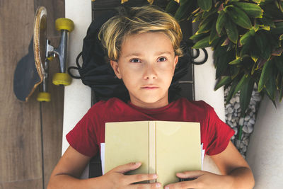 Directly above portrait of boy with book lying down outdoors