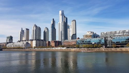 Modern buildings by river against sky in city