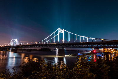 Illuminated bridge over river against sky at night