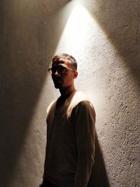 Young man wearing sunglasses standing against wall