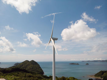 Wind turbine by sea against sky