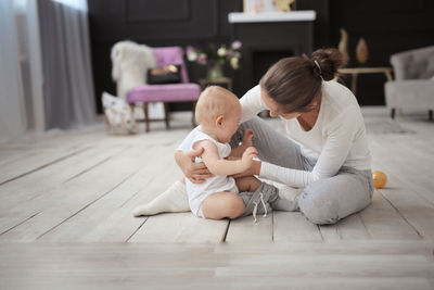 Mom changes clothes crying baby of 10 months on the floor in a cozy real light interior.