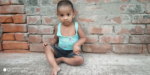 Full length of girl sitting against brick wall