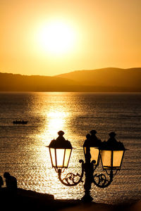 Silhouette people on sea against sky during sunset