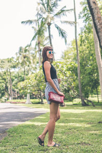 Woman wearing sunglasses standing by plants against trees