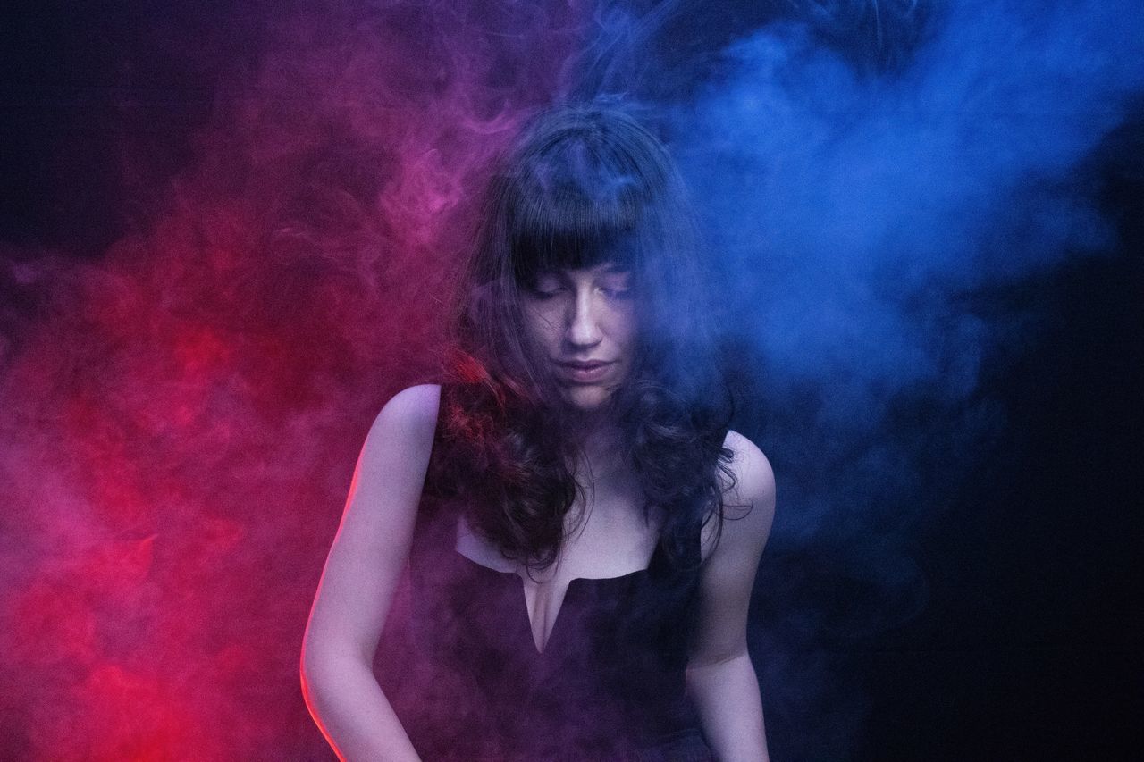 smoke - physical structure, young adult, one person, hairstyle, front view, leisure activity, young women, long hair, hair, waist up, real people, indoors, casual clothing, lifestyles, portrait, adult, standing, beautiful woman, black background