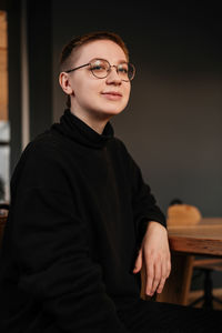 Young woman with short hair in eyeglasses and black sweater sitting at the table in office