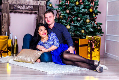 Portrait of young couple on rug by decorated christmas tree at home