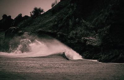 Sea waves splashing on rocks against sky