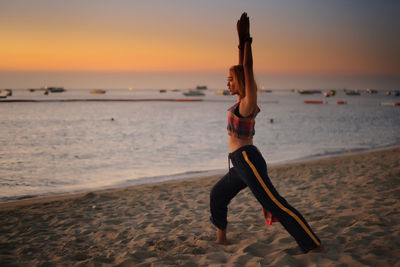 Full length of woman exercising at beach during sunset