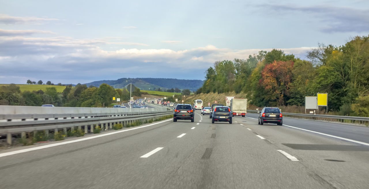 VEHICLES MOVING ON ROAD AGAINST SKY