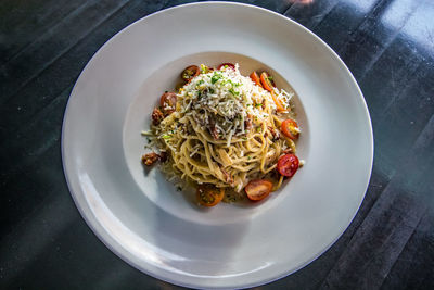 High angle view of pasta in white plate on table with tomato parmesan cheese fresh herbs and noodles