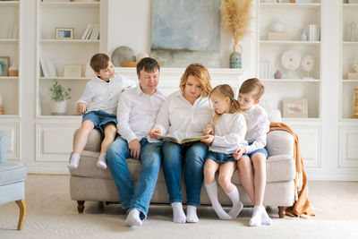 Happy family reading book at home. mom and dad and young children sit together
