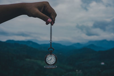 Close-up of hand holding clock against sky