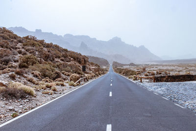 Empty road leading towards mountains against sky