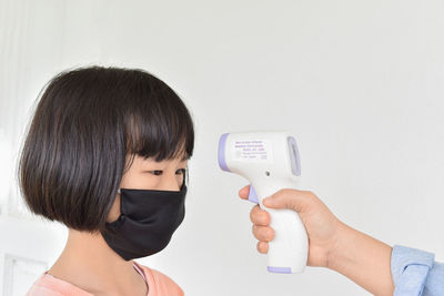 Portrait of woman holding camera against white wall