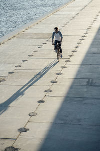 Young man riding bike on waterfront promenade at the riverside