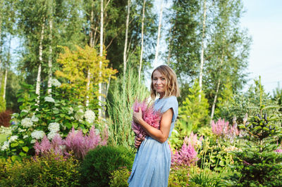 Portrait of smiling young woman standing by purple flowering plants