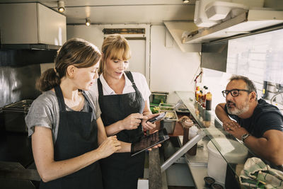 Female chefs with technologies while receiving order from man in food truck