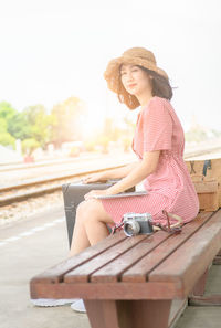 Portrait of young woman sitting on bench at railroad station