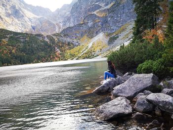 Man on rocks by river against mountains