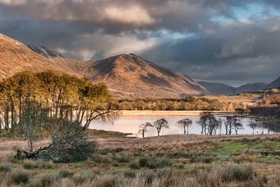 Scenic view of lake by mountains against dramatic sky