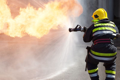 Rear view of firefighter spraying water on fire