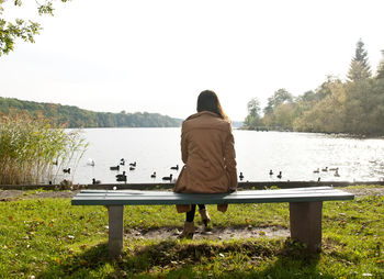 Rear view of woman sitting on bench at lakeshore