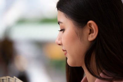 Close-up of young woman looking at paper currency against defocused background