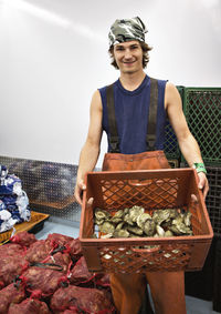 Portrait of man holding oyster container while standing in fishing industry