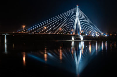 Illuminated bridge over river against sky at night