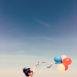 Low angle view of woman holding helium balloons against sky