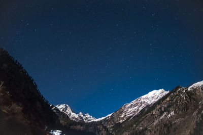 Low angle view of snowcapped mountains against clear blue sky