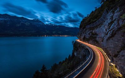Light trails on road by mountain against sky at dusk