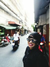 Portrait of smiling young woman on street amidst buildings in city