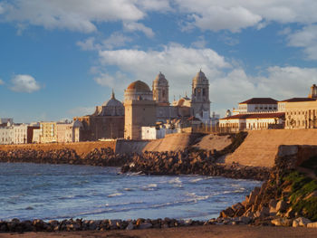 Buildings by sea against cloudy sky
