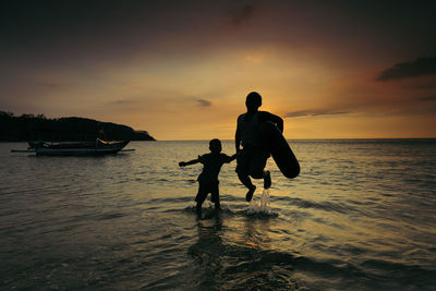 Silhouette children on beach against sky during sunset