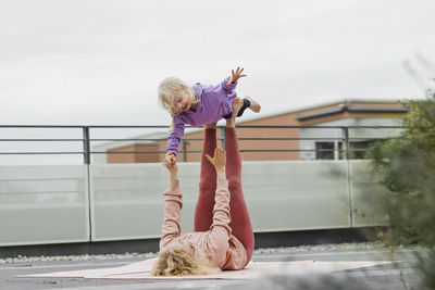 Mother balancing girl on legs lying down at rooftop