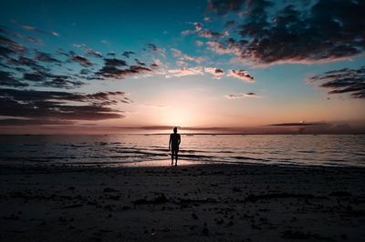 Silhouette person standing on beach against sky during sunset