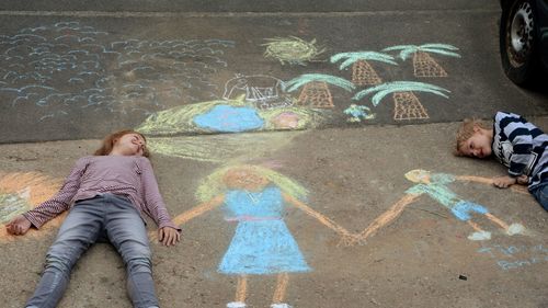 High angle view of siblings lying on chalk drawings at footpath