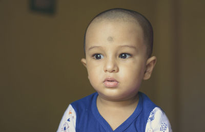 Cute bald indian baby boy in blue and white shirt looking away. head and shoulder shot. close up.