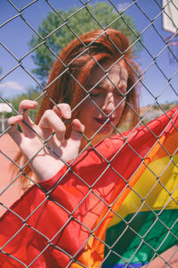 Young woman with rainbow flag seen through chainlink fence