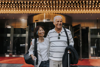Happy male and female senior friends standing in front of movie theater