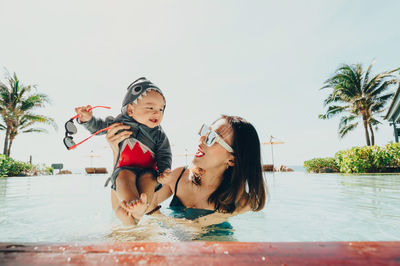 Smiling mother with son in swimming pool against sky