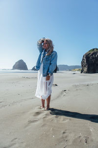 Young woman with hand in hair standing at beach against clear sky