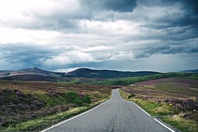 Road passing through landscape against cloudy sky