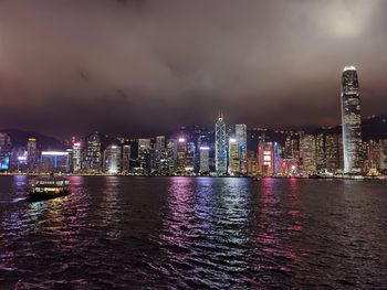 Illuminated buildings by river against sky at night