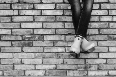 Crossed legs of a young girl in jeans and galoshes sitting on a brick wall