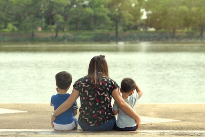 Rear view of mother with sons sitting by lake in park