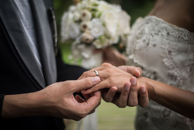 Midsection of bride and groom exchanging rings while holding hands